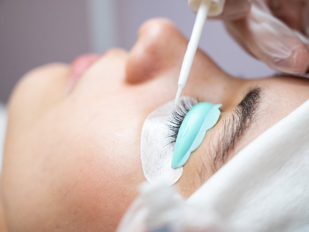 Young woman undergoing eyelash tinting and lamination procedure.